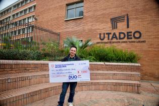 Estudiante tadeísta ganador del torneo frente a los arcos de Utadeo sosteniendo el cheque