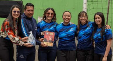 Cuatro integrantes del equipo femenino de fútbol sala posan junto al trofeo, el director de deportes y la jefe de la Oficina de Egresados