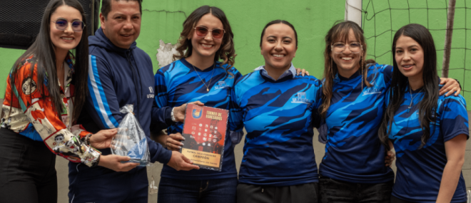 Cuatro integrantes del equipo femenino de fútbol sala posan junto al trofeo, el director de deportes y la jefe de la Oficina de Egresados