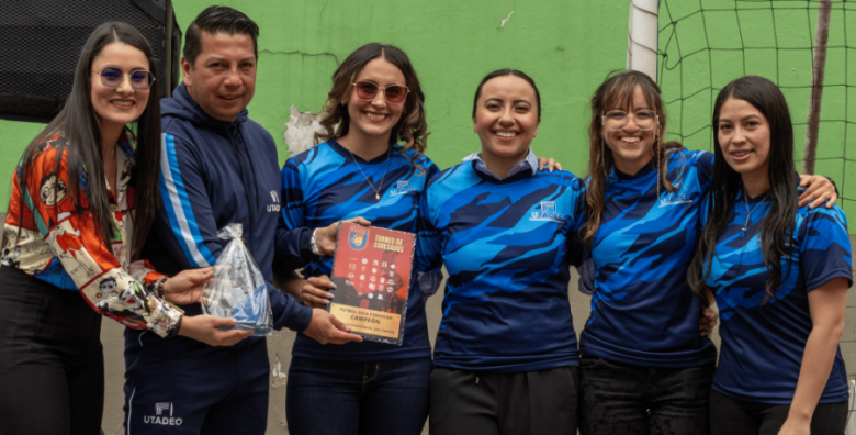 Cuatro integrantes del equipo femenino de fútbol sala posan junto al trofeo, el director de deportes y la jefe de la Oficina de Egresados